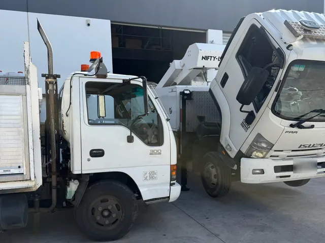 Isuzu truck with its cab tilted forward for engine access, beside the service truck